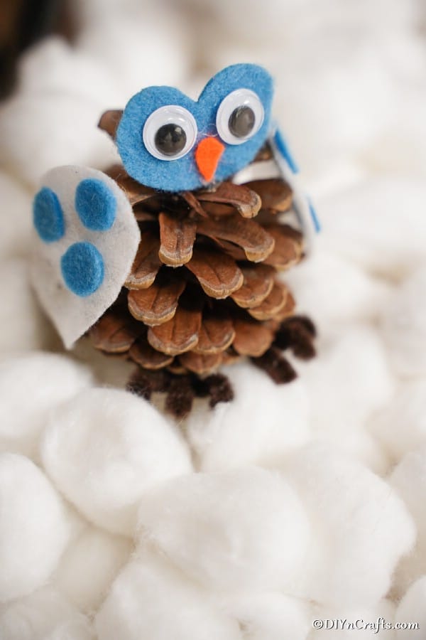 A pinecone owl decoration sitting on a bed of cotton balls