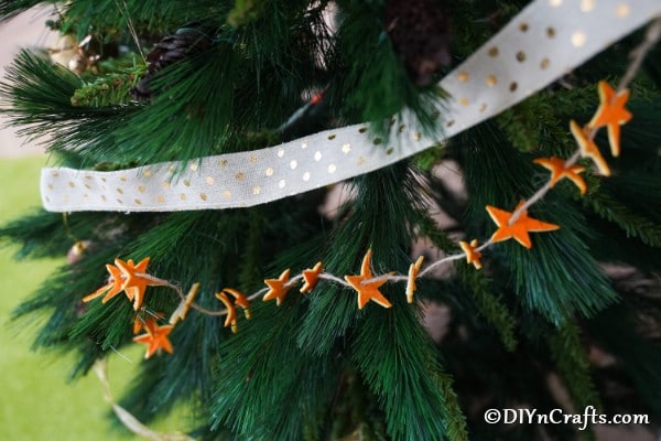 Up close picture of an orange star garland hanging on a Christmas tree