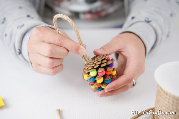Adding a loop of twine for the ornament hanger to the top of a pinecone ornament