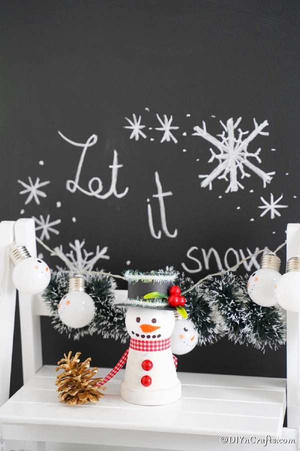 Clay pot snowman decoration on a white shelf in front of chalkboard let it snow sign