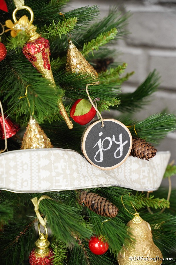 A wood slice chalkboard ornament hanging on the Christmas tree