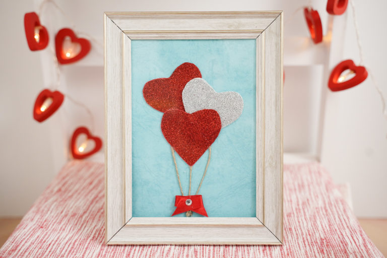 Framed heart balloons decoration on stool with red heart garland in background
