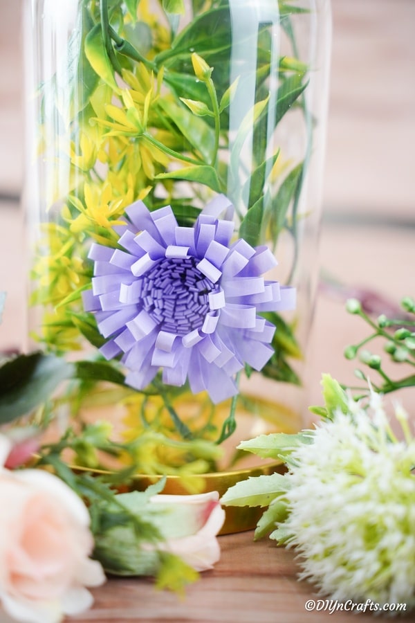 A purple paper flower inside a jar with greenery