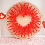 Heart string art in front of white wall with paper heart garland