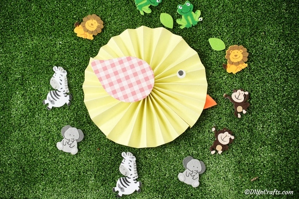Paper bird kids craft on grass surrounded by mini toy animals
