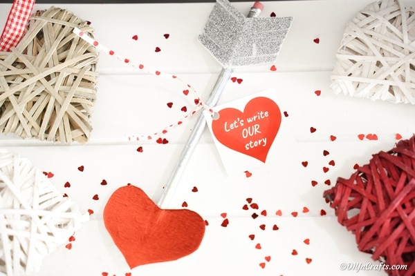 Valentine pencil on white paper with red confetti hearts