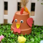 Flower pot chicken on grass in front of white fence