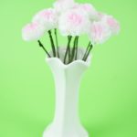 Tissue paper flowers in white vase on green background