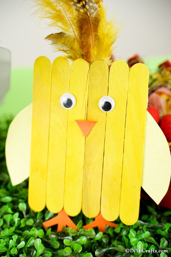 Yellow popsicle stick chick leaning against grass