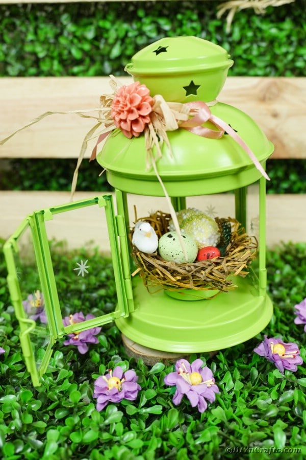 Green lantern easter craft on grass by wooden box
