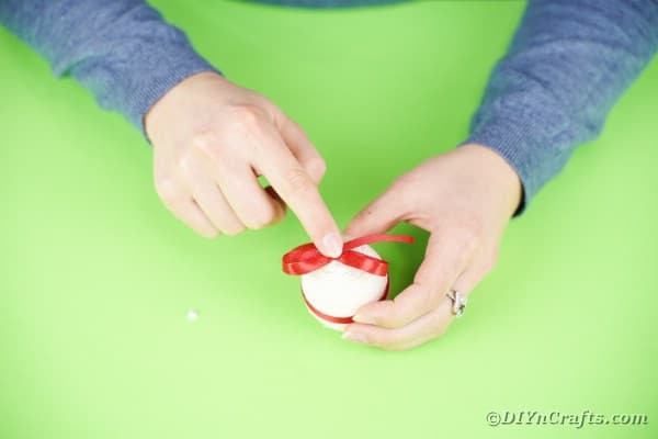 Gluing red bow to top of egg