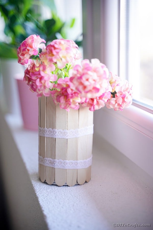 Craft stick can with pink flowers on windowsill