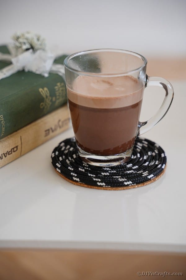 Glass of coffee on black coaster on side table by books