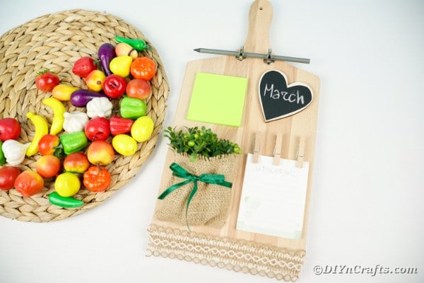 Cutting board memo station next to plastic fruit on woven mat