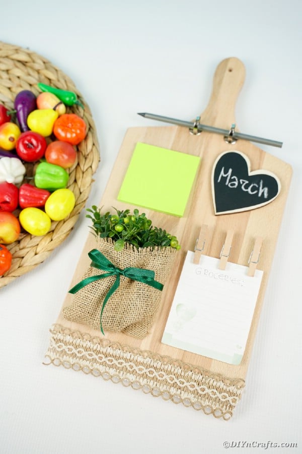 Cutting board memo station next to plastic fruit on woven mat