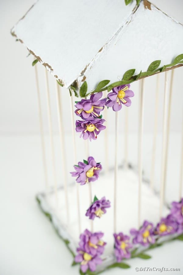White birdcage with purple flowers on white surface