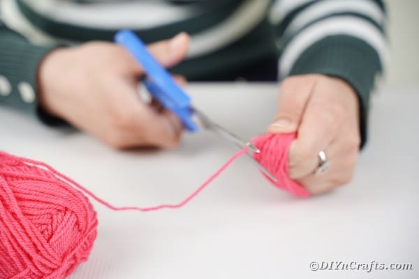Cutting end of pink yarn off hand