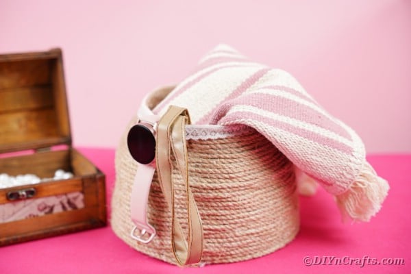 Rope basket with blanket inside on pink surface