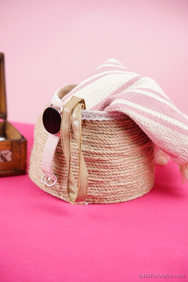 Rope basket with blanket inside on pink surface