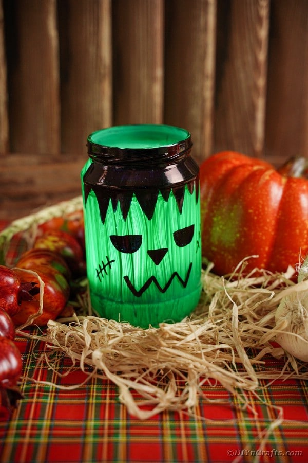 Frankenstien lantern with candle by pumpkin and hay