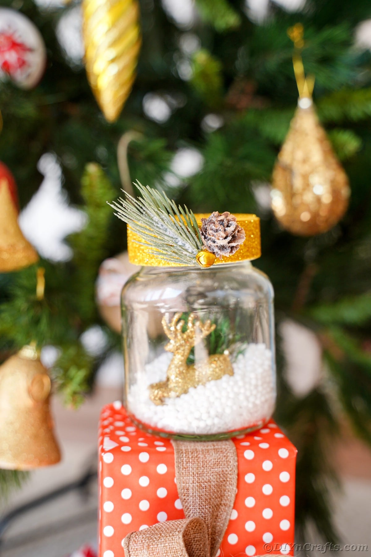 snow globe with gold top on red and white gift by tree