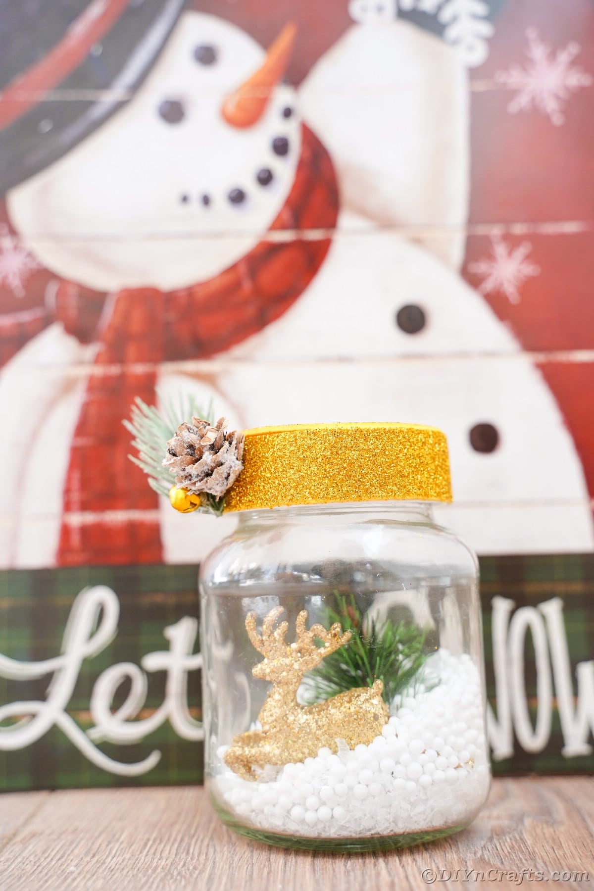 let it snow snowman sign with a small jar with snow and gold cap in front