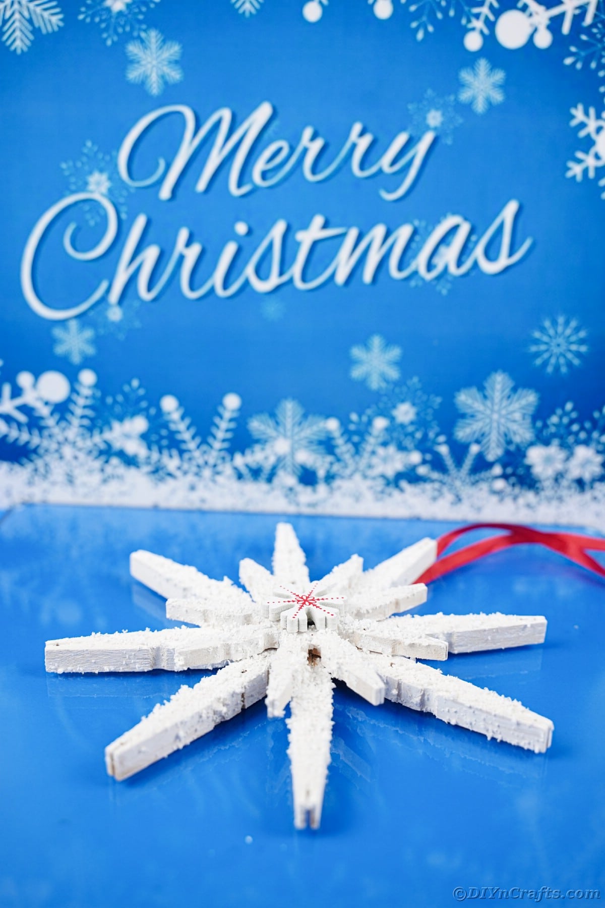 white clothespin snowflake laying on blue table with merry christmas message above