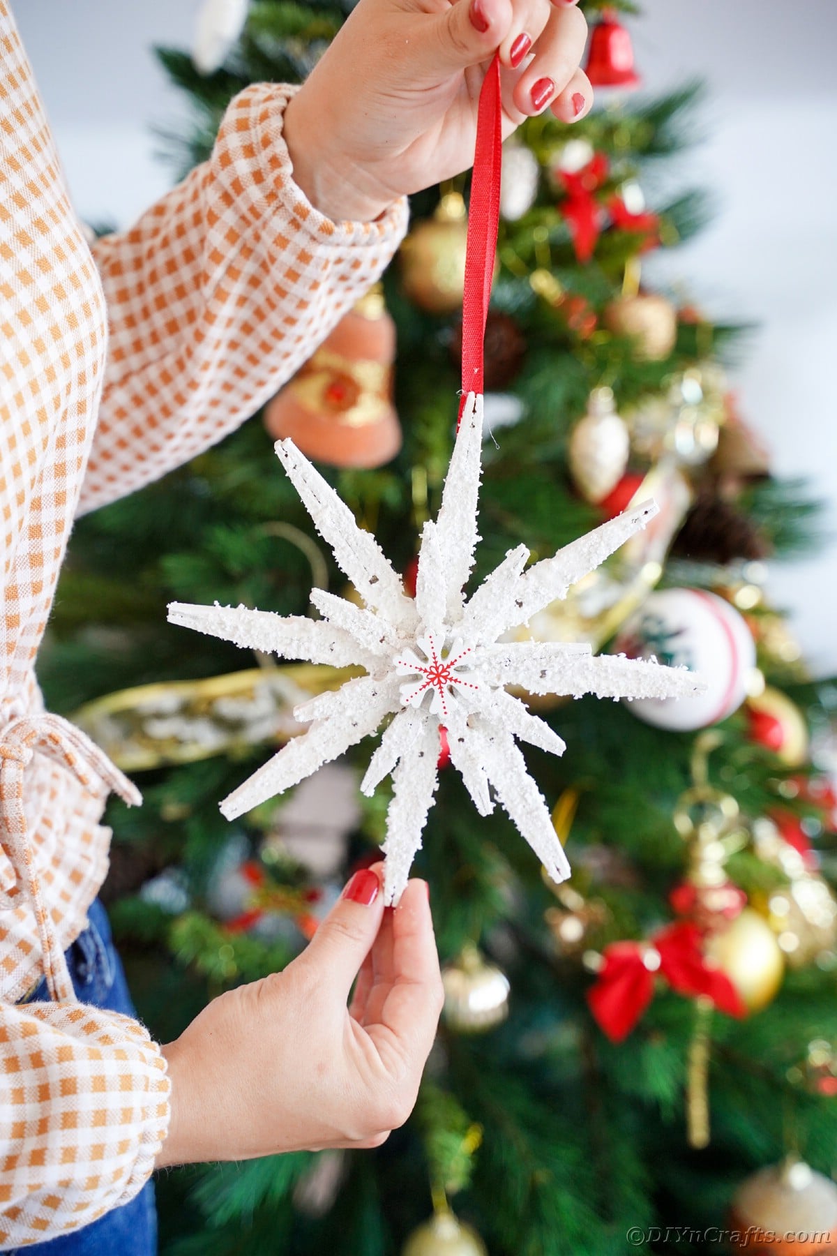 woman holding clothespin snowflake in front of tree