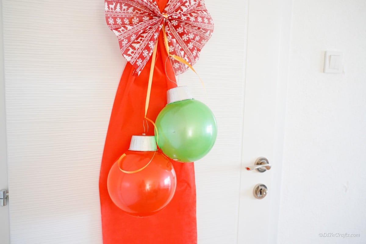 Large Christmas ornaments hanging from door with ribbon