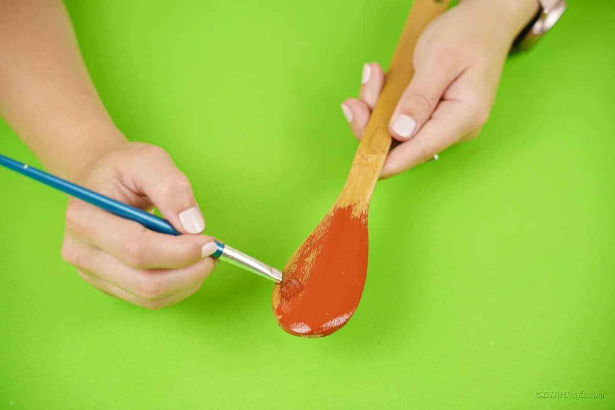 Painting red paint onto a wooden spoon Christmas craft