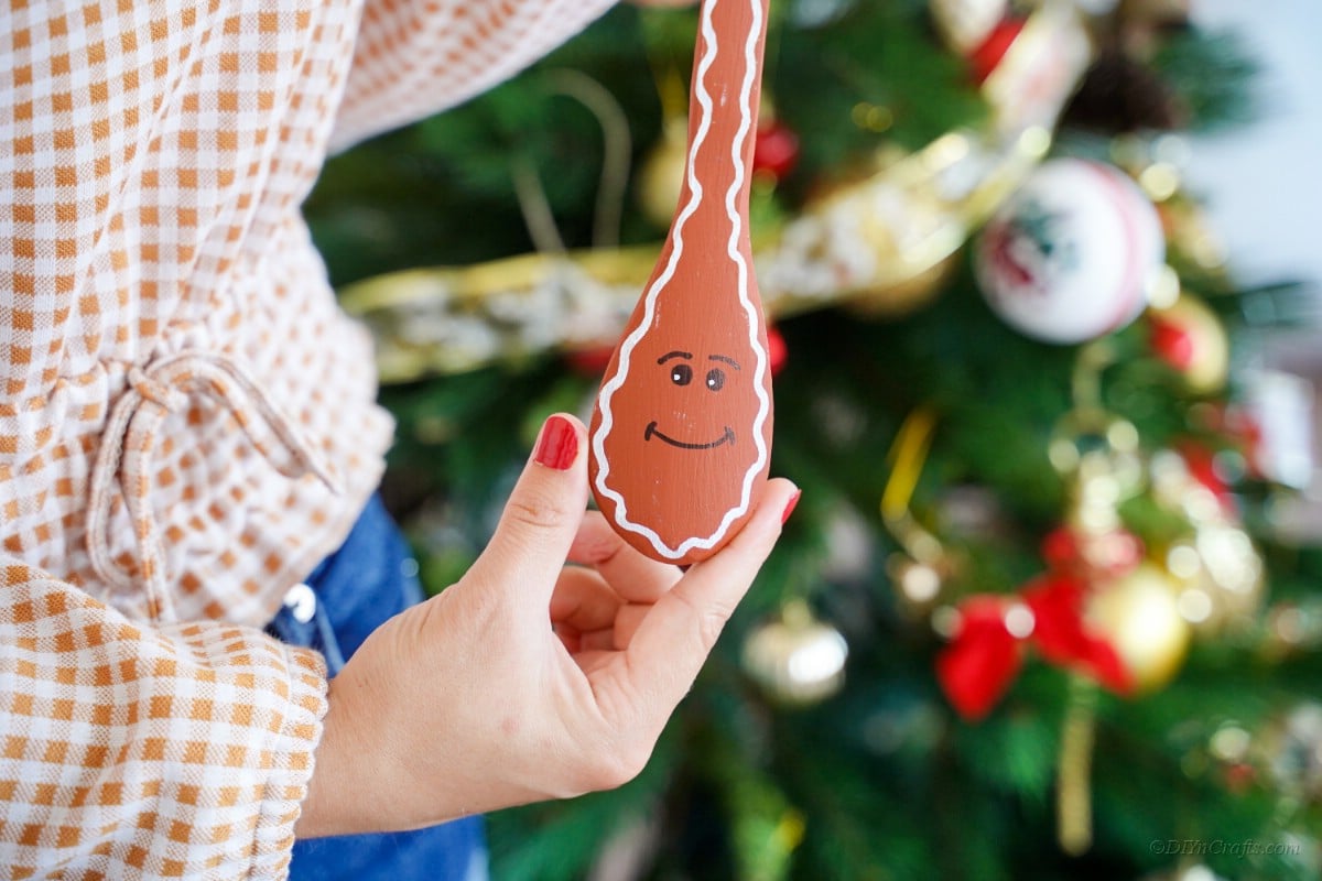 Woman holding painted spoon in front of Christmas tree