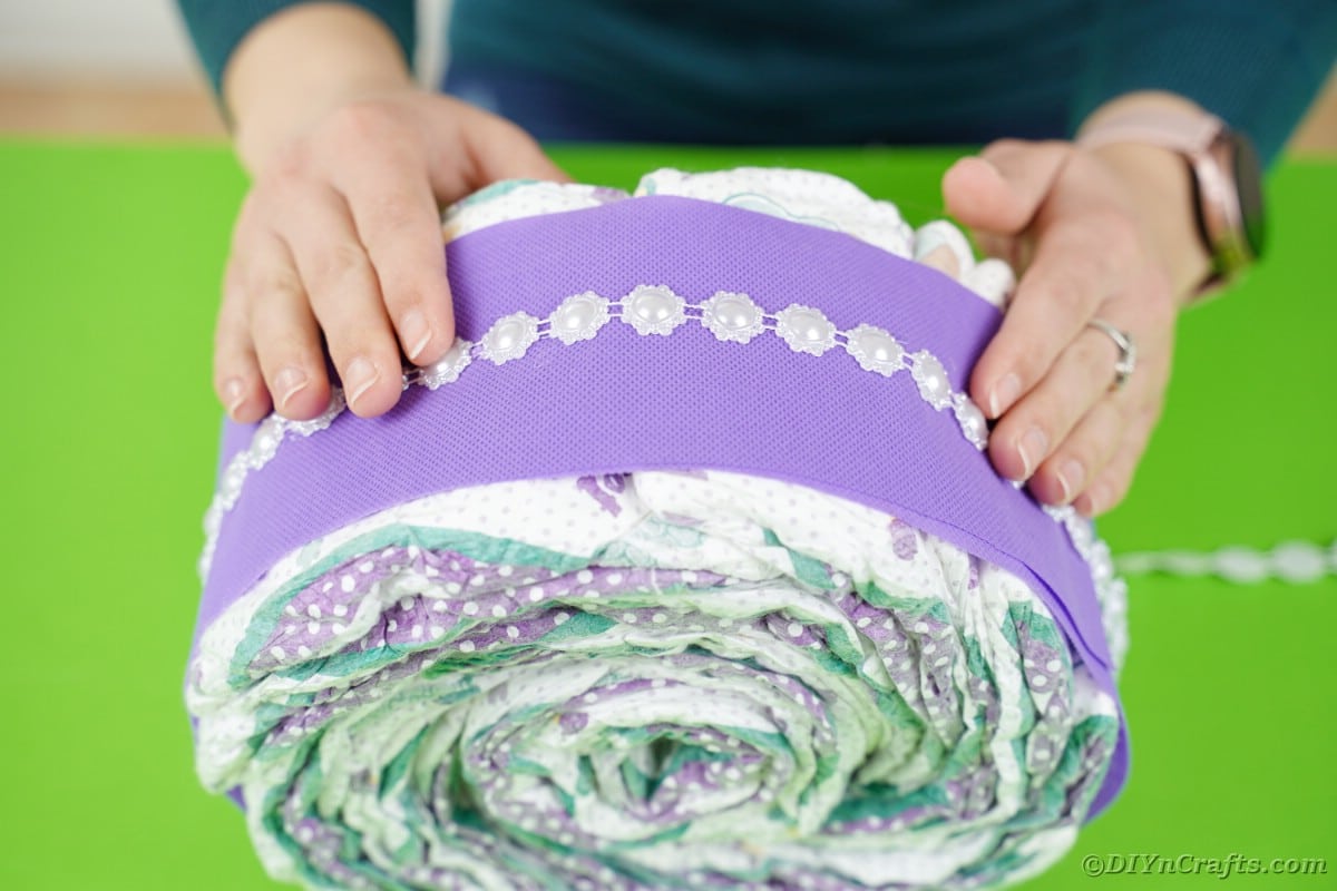 Gluing beaded ribbon around diaper cake