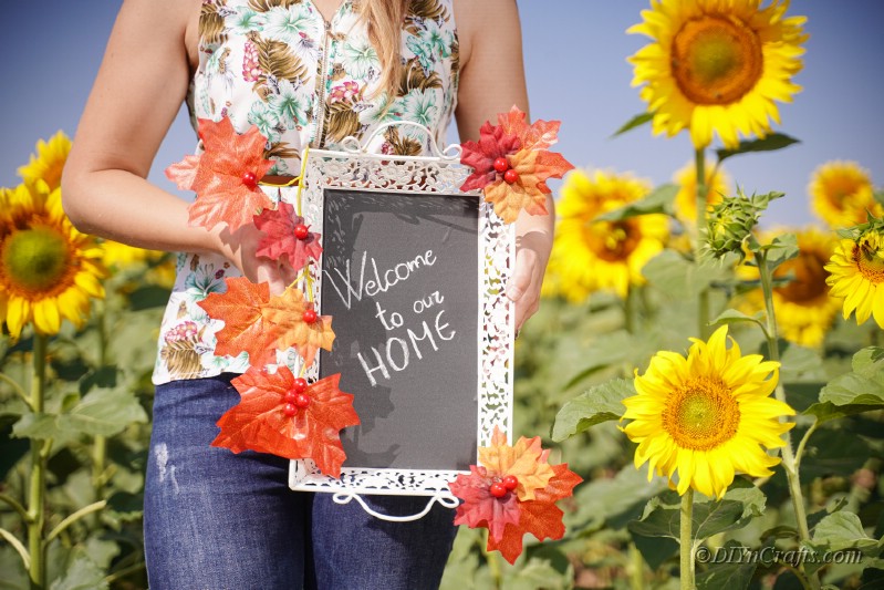 woman holding fall themed sign in sunflower field 