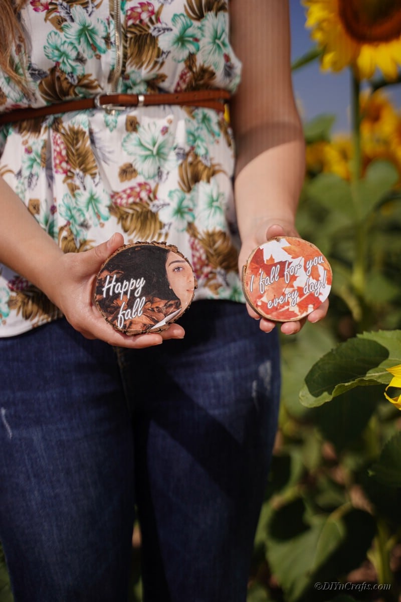 Woman in floral shirt holding wood slice photos in hands next to sunflowers