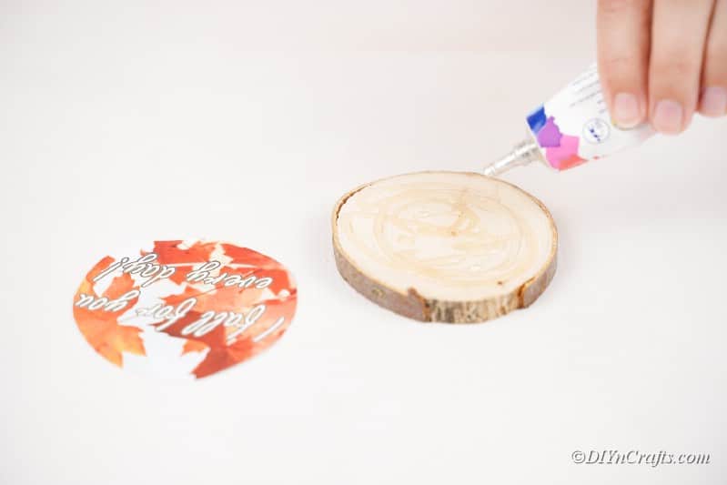 Hand holding glue above wood slice with fall picture on table