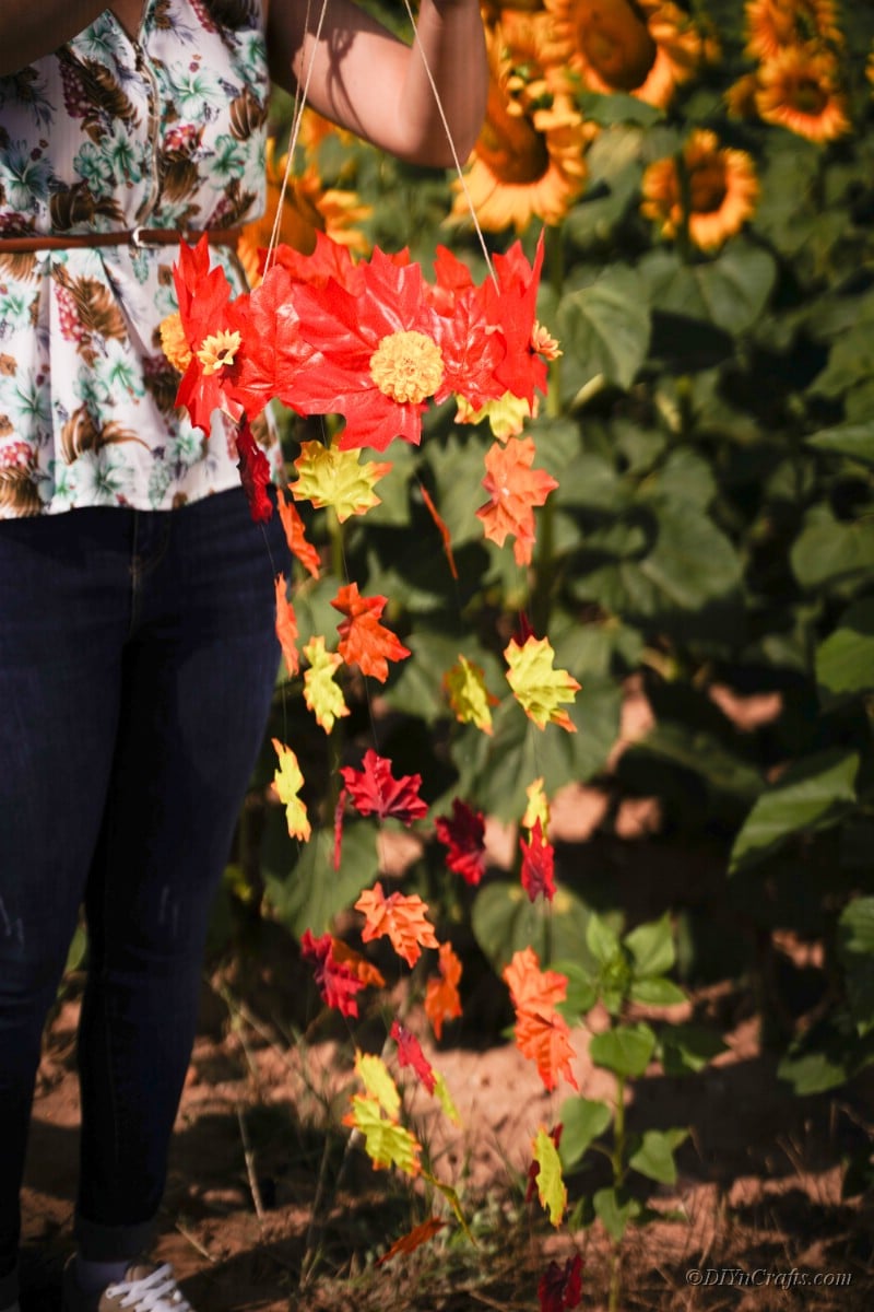 Frau in Jeans hält Herbstblattmobile vor Sonnenblumenfeld