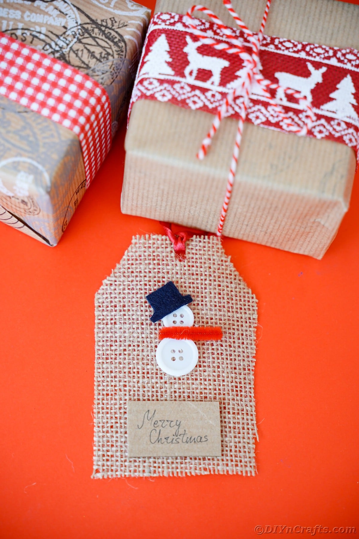 snowman gift tag laying on red table by brown gift