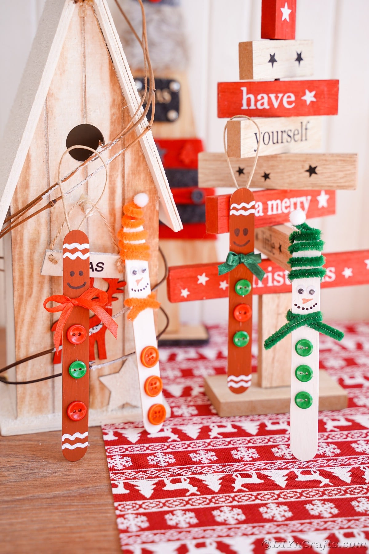 four craft stick ornaments standing up in front of wood Christmas decorations