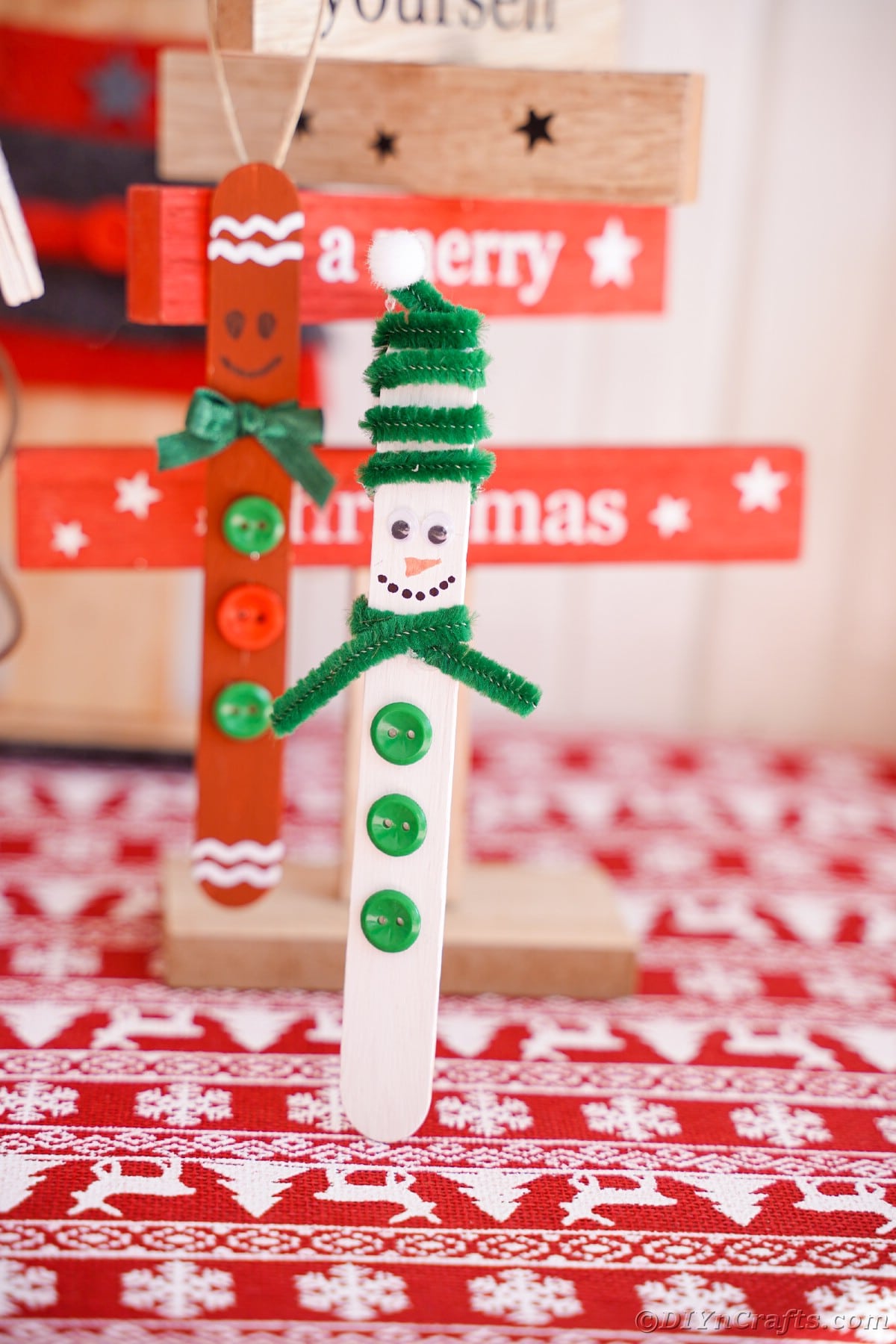 gingerbread and snowman craft stick ornaments in front of holiday decor