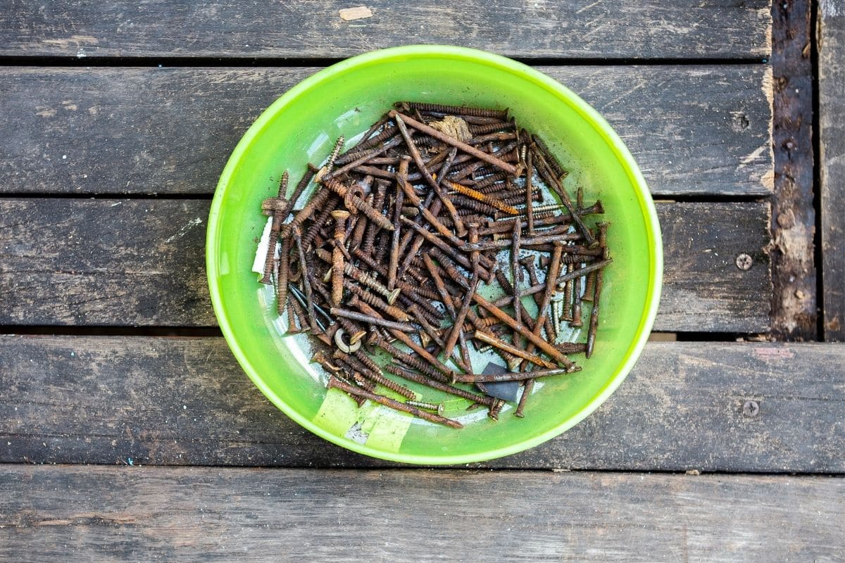 rusty nails in a green bowl placed in the wooden table