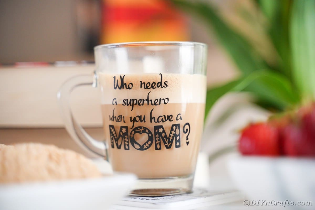 Glass mug with superhero mom message next to cookies