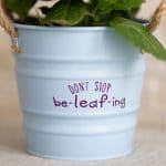White flower pot with purple message that says don't stop be leaf ing