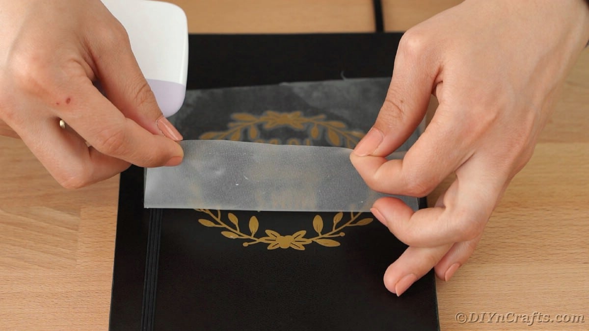 Peeling transfer tape off gold foil on black book