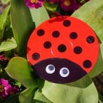 Upcycled CD ladybug craft sitting on plant with pink flowers
