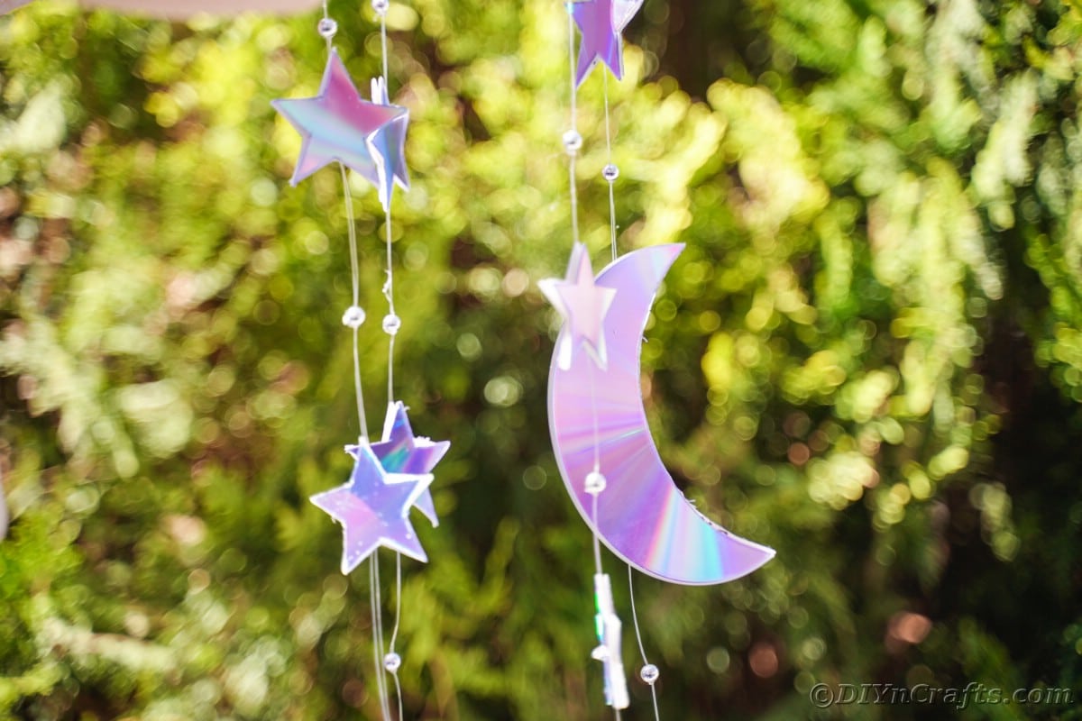 CD cut into star and moon strung on fishing line in front of shrub