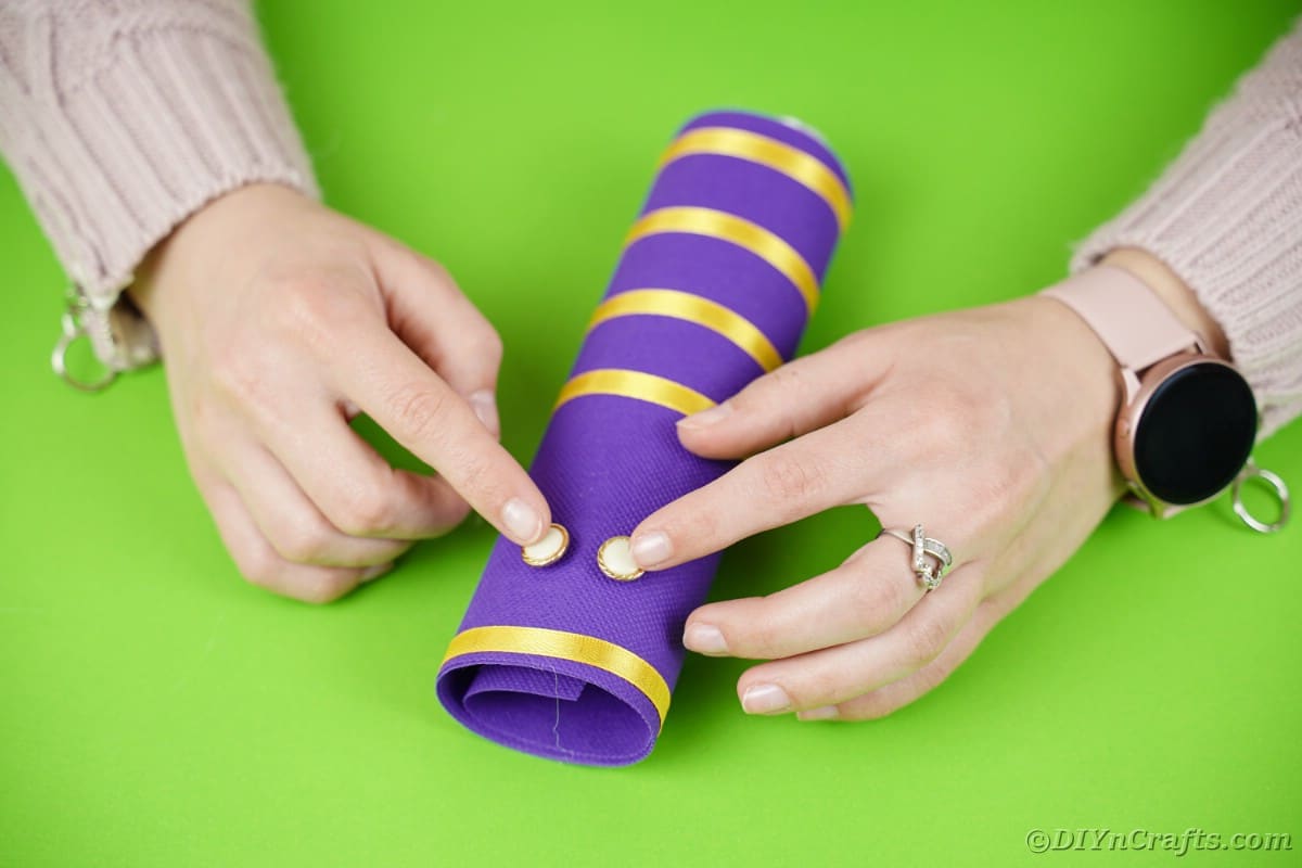 Gluing button eyes onto purple tube with yellow stripes