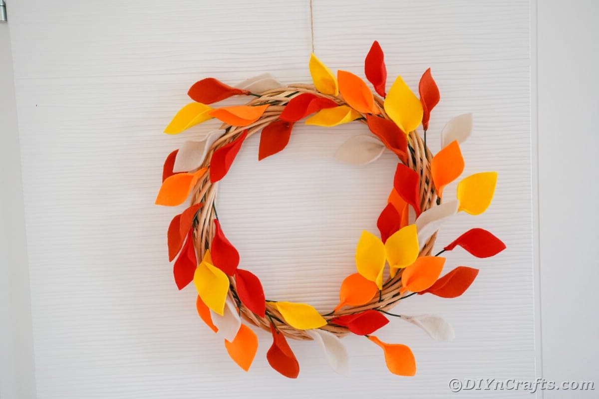 Orange and yellow fake leaves on grapevine wreath hanging on white door