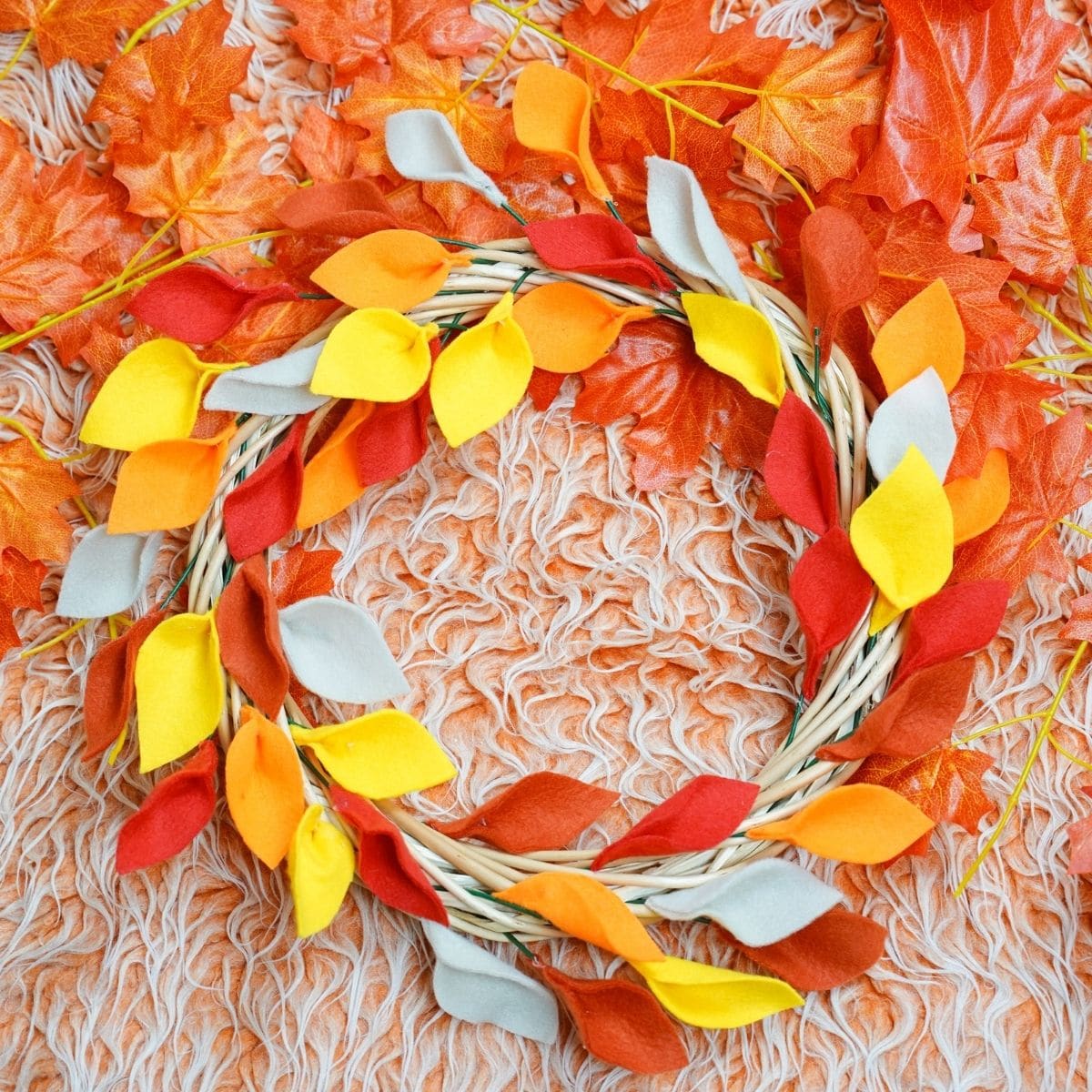 Fall leaf wreath on orange rug surrounded by fake leaves