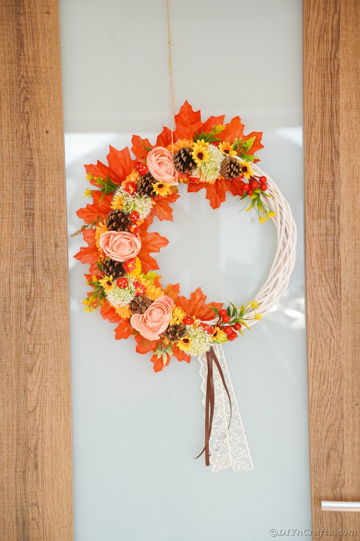 Orange flowers and pinecones on white wreath on door