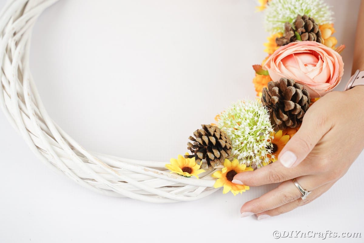 Hand putting sunflowers on white wreath by pinecones